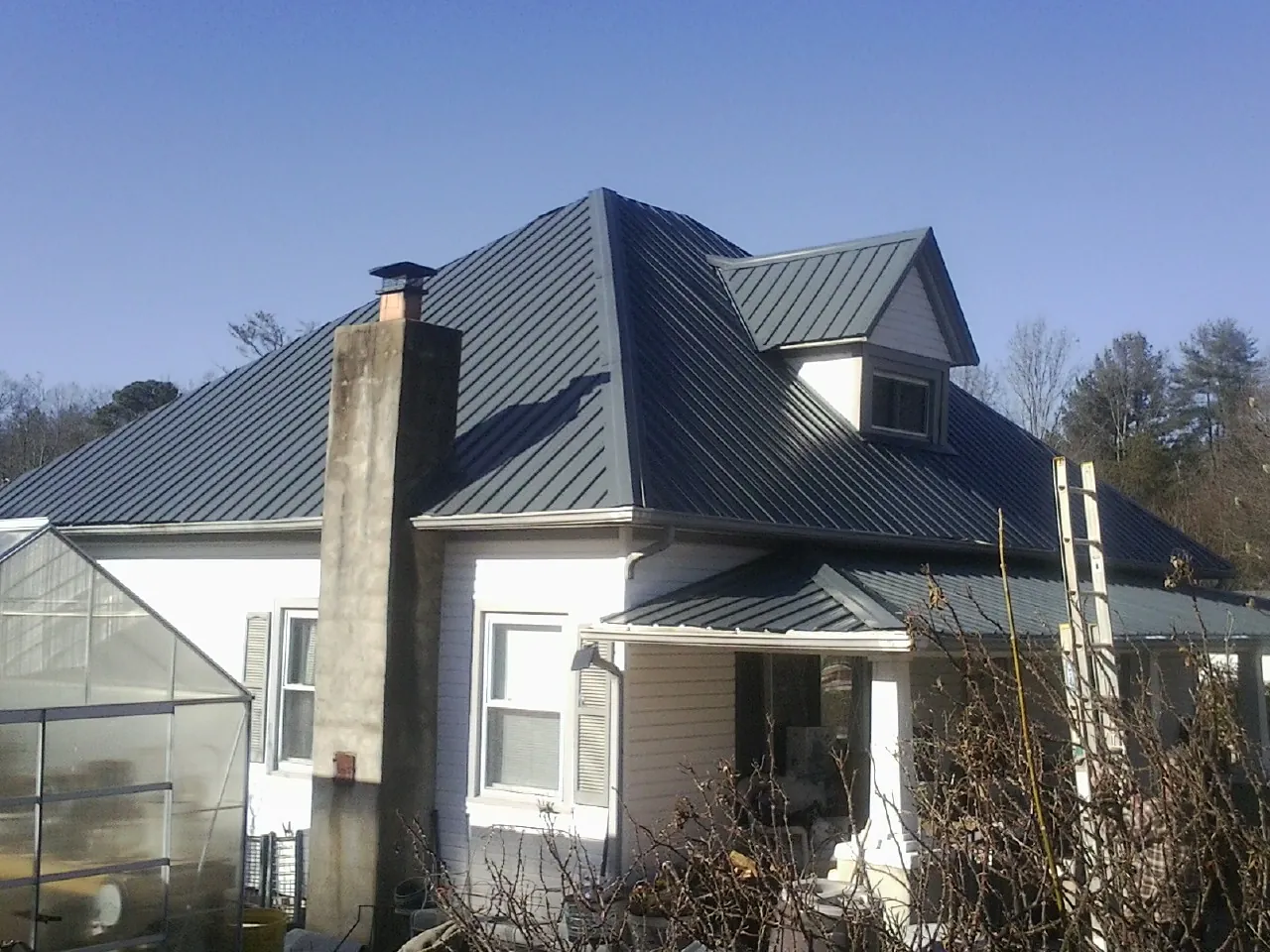 Dark blue standing seam metal roof on a white farmhouse with dormer — Slate & Tile Roof Repair by Roofing Brothers in Locust