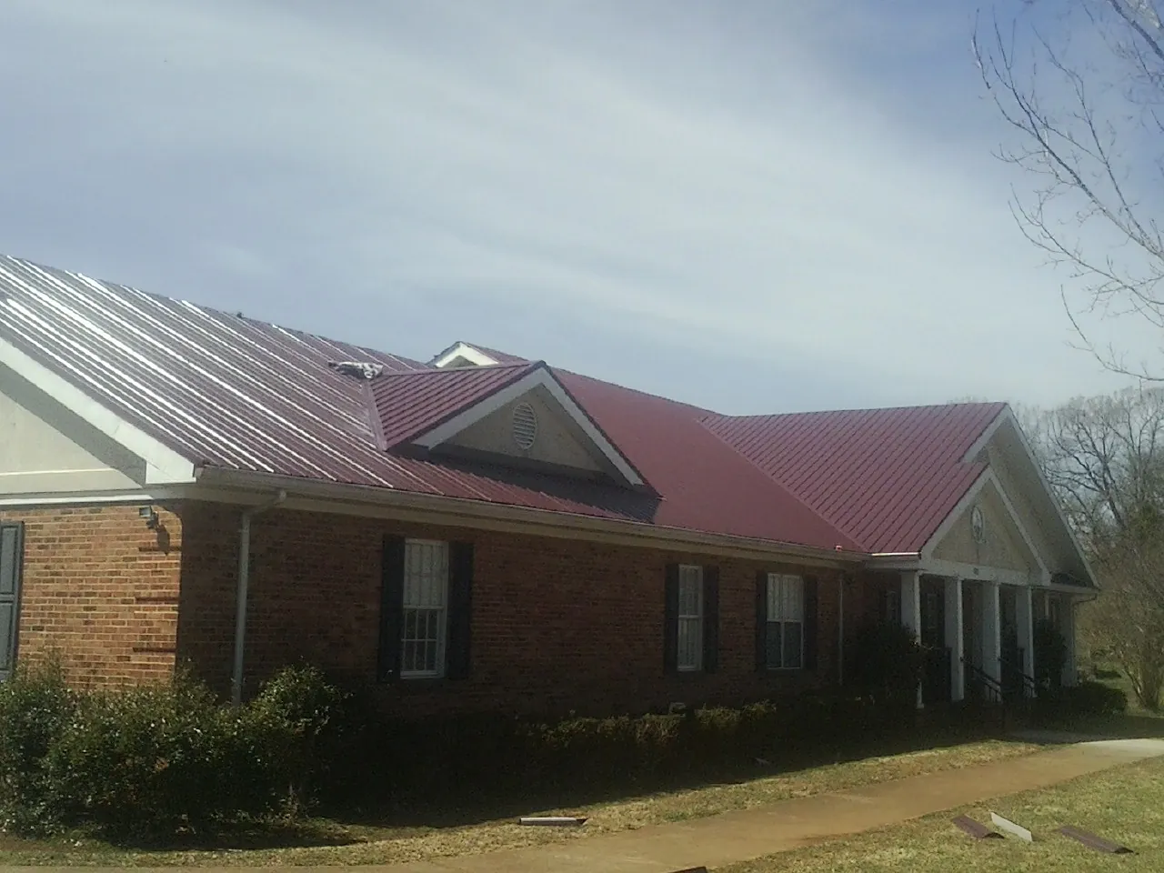 Red metal roof with gabled entries on a long brick building, from a Hail Damage Roof Repair job in Locust