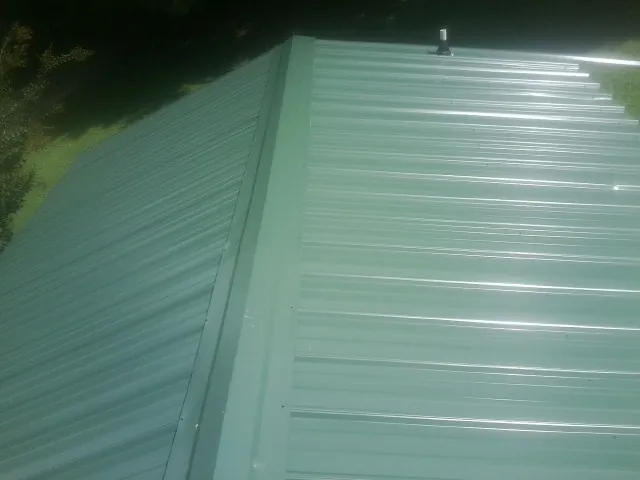 New green metal panels meeting at the ridge of a roof — Flat Roof Repair work by our crew in Locust