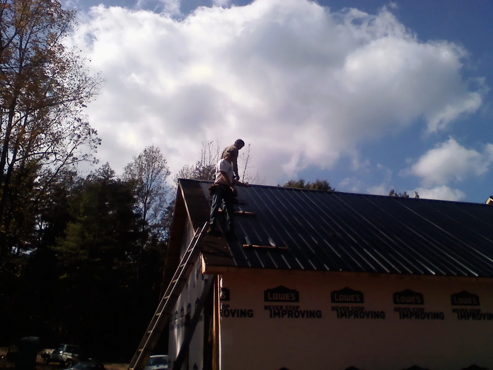 Roofer fastening dark metal panels high against a cloudy sky, from a Roof Inspection job in Locust
